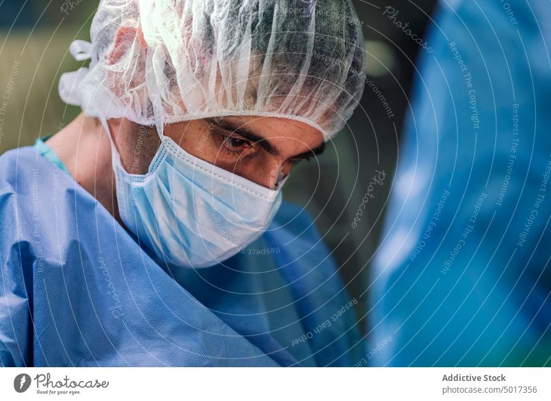 Crop man surgeon in mask and surgical cap during operation sterile serious concentrate focused thoughtful specialist clinic doctor occupation medic male work