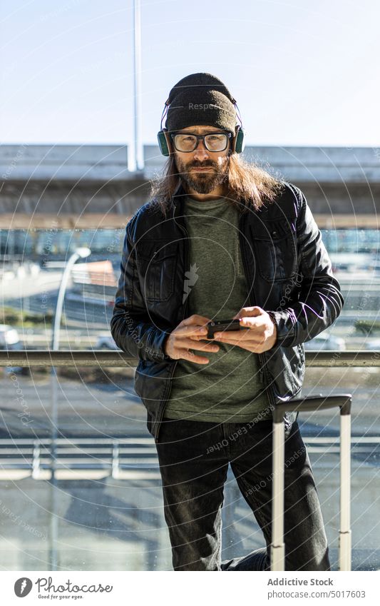 Hipster man browsing smartphone in airport watching travel passenger trendy style hipster adult smile positive modern serious male beard hat leather jacket