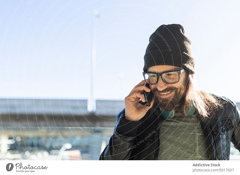 Hipster man talking on phone in airport travel passenger trendy style smartphone hipster adult smile positive modern serious male beard hat leather jacket black