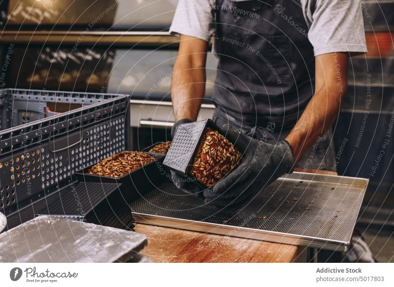 Crop male cook with baked bread fresh man baking pan prepare crust tasty delicious aromatic apron baker cuisine sunflower seed metal tray kitchen bakery