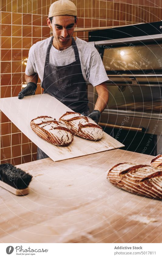 Smiling male cook with bread in bakery man wooden table bakehouse baked fresh tasty oven smile cheerful loaf food pastry delicious apron cuisine culinary guy