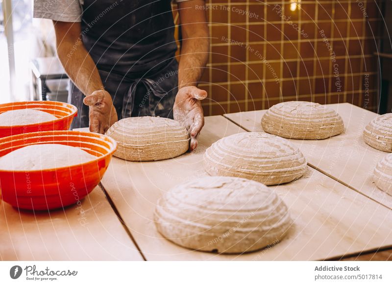 Crop male cook shaping dough with proofing basket prepare man baker bakery raw bread shape apron wooden table manufacture process production kitchen food fresh
