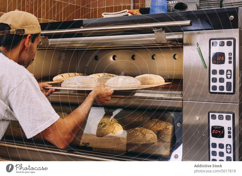 Male cooking bread in bakery oven man kitchen dough industrial male tray apron pastry prepare food fresh culinary work chef job uniform guy recipe occupation