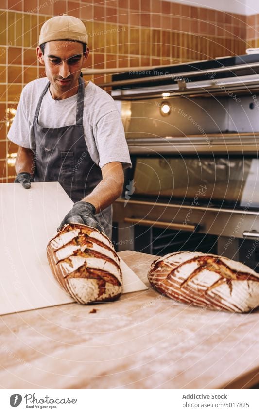 Smiling male cook with bread in bakery man wooden table bakehouse baked fresh tasty oven smile cheerful loaf food pastry delicious apron cuisine culinary guy