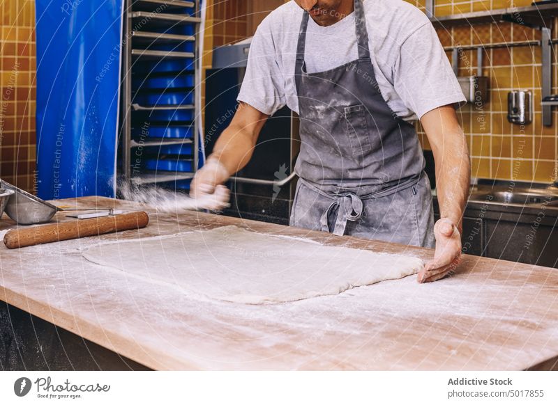Crop cook sprinkling flour on dough sprinkle baker man process prepare raw scatter male bakehouse dirty bakery apron table food work recipe job fresh occupation