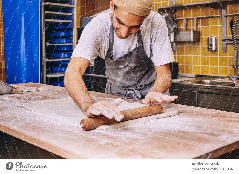 Crop male cook rolling dough in bakery rolling pin man prepare raw bakehouse table dirty flour ingredient apron culinary cuisine chef fresh food guy kitchen