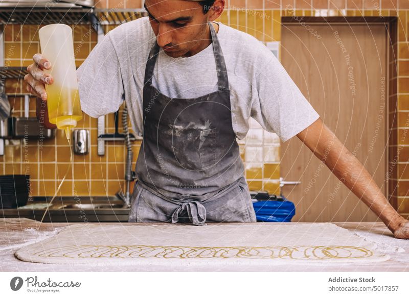 Male baker pouring oil on raw dough bakery man cook process prepare recipe male cuisine apron table work flour food kitchen professional pastry culinary guy