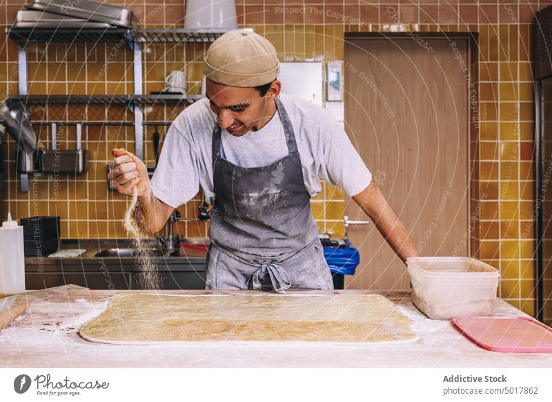 Cook sprinkling flour on dough sprinkle baker man cook process prepare raw scatter male bakehouse dirty bakery apron table food work recipe job fresh occupation