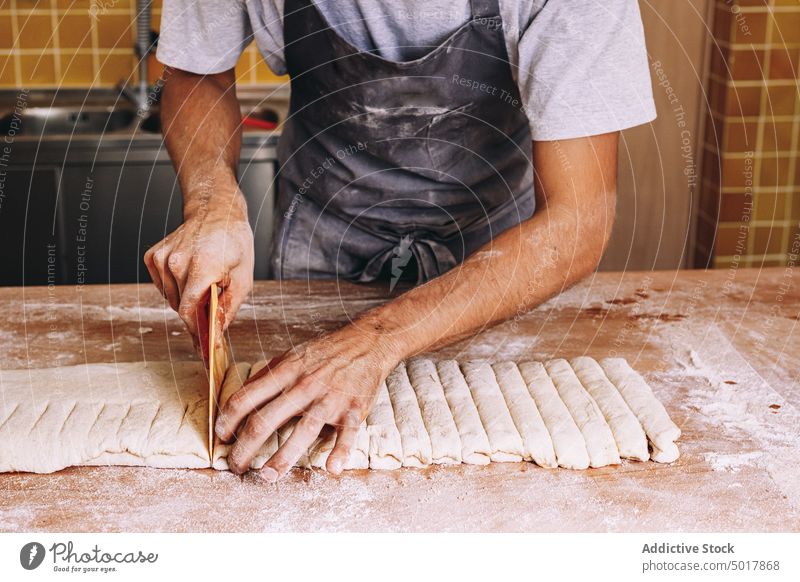 Crop male cook cutting dough on table raw piece man bakery process apron wooden pastry work cuisine food ingredient uncooked professional recipe job flour guy