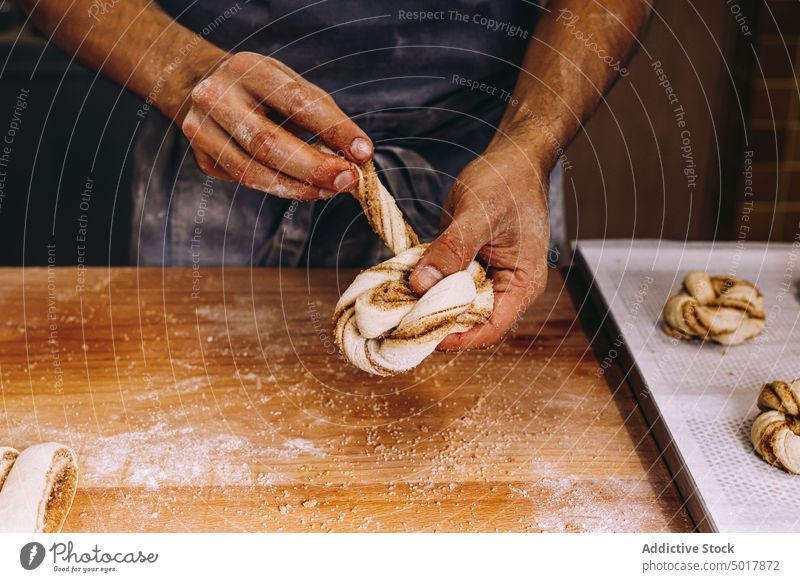 Male baker cooking cinnamon rolls dough prepare man bun raw uncooked shape process male bakery flour table wooden apron stand fresh kitchen cuisine culinary guy