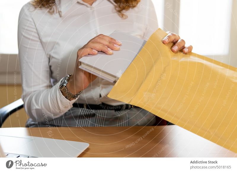 Anonymous ethnic businesswoman with diary and envelope against laptop agenda professional friendly office using device sincere gadget put content internet