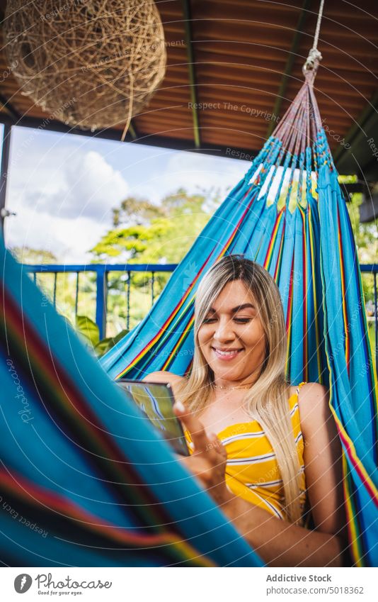 Smiling woman browsing smartphone and resting in hammock using chill toothy smile cheerful terrace resort relax veranda mobile summer lounge vacation