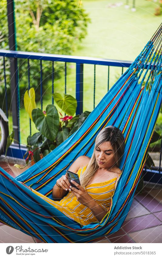 Woman browsing smartphone and resting in hammock woman using chill terrace resort relax veranda mobile summer lounge vacation social media app surfing young