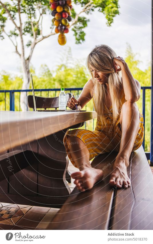 Positive woman using smartphone and laptop on terrace veranda garden positive summer browsing casual cellphone young park device gadget mobile online touch hair
