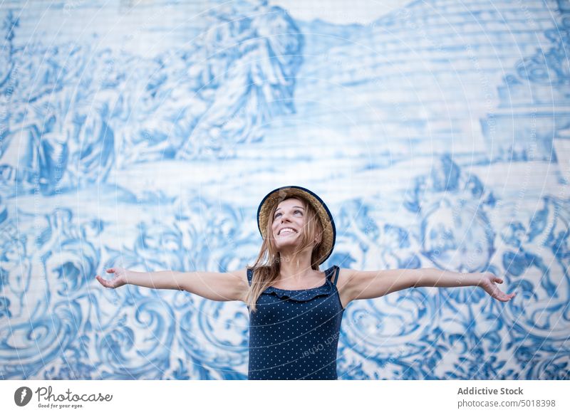 Content female tourist against wall with mural in town traveler fresco art freedom glad outstretch enjoy feminine woman old smile content happy cheerful