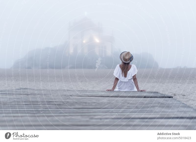 Anonymous traveler contemplating chantry and sea in mist from dock contemplate ocean pier vacation solitude idyllic woman rest fog weather haze chapel sky trip