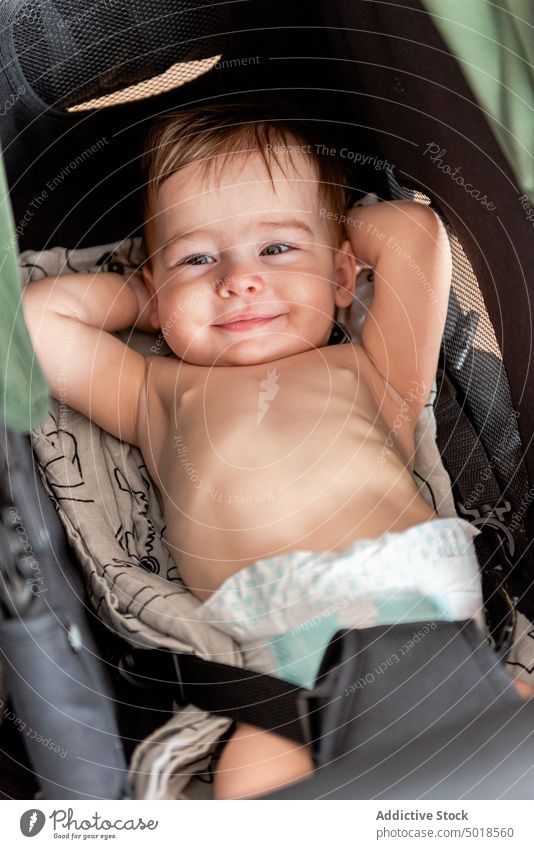 Funny infant lying in stroller with hands behind head baby smile happy hand behind head adorable shirtless joy rest cute cheerful innocent childhood babyhood