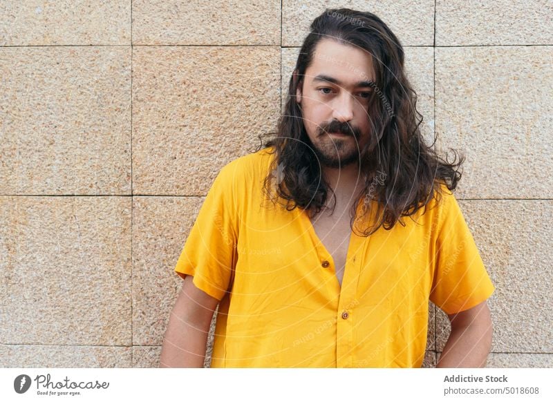 Portrait os stylish man with long hair in city hipster beard style appearance wavy hair summer outfit bright male arms crossed trendy handsome shirt street