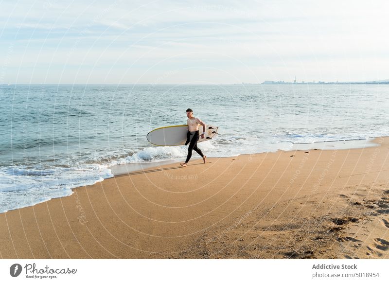Young man with surfboard walking on beach surfer sea wave active sporty summer ocean shirtless male young shore seashore activity sand vacation athlete seaside