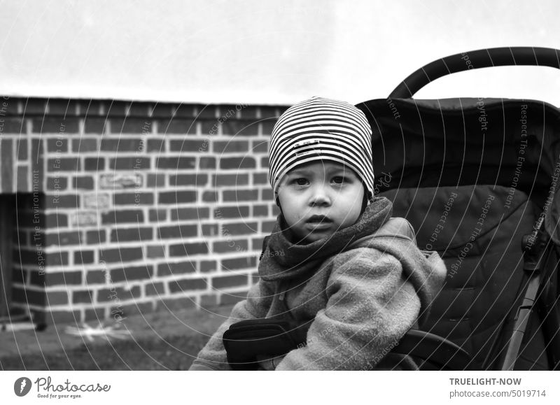 Energy crisis? A child barely two years old sits warmly wrapped up with cap, scarf, fleece jacket in his buggy and looks very seriously and questioningly directly into the camera