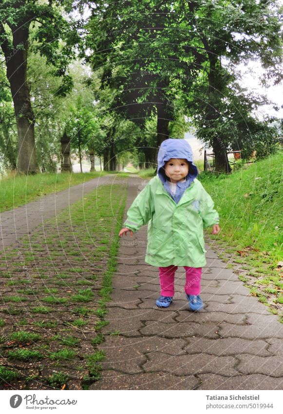 Little girl walking along avenue Girl rainy Rain Rain jacket Child Rubber boots hood Green Human being Exterior shot Bad weather Wet Infancy Playing Boots trees