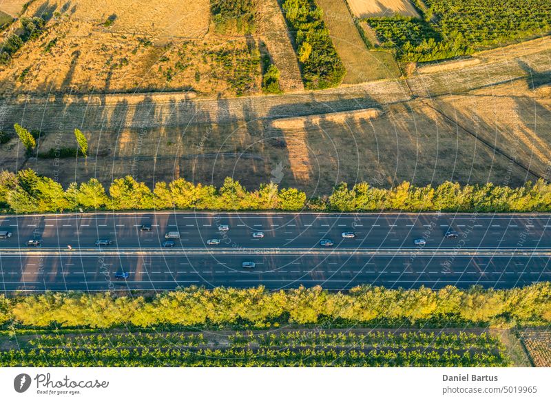 Highway from a bird's eye view. As the sun goes down, the sun's rays create beautiful long shadows on the ground. Yellow trees and surrounding farmland aerial
