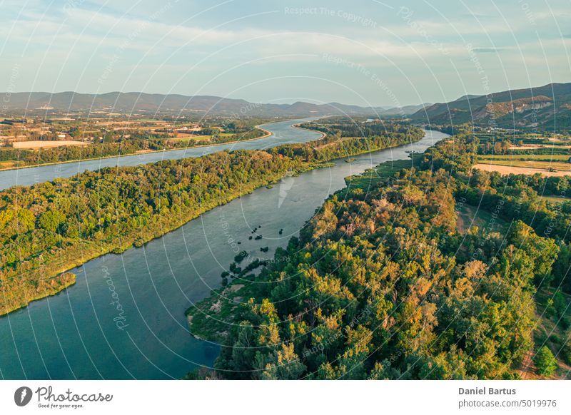 Aerial view of the Rhone River in southern France. A naturally formed island in the middle of the river. Covered with forests with a view of the surrounding mountains