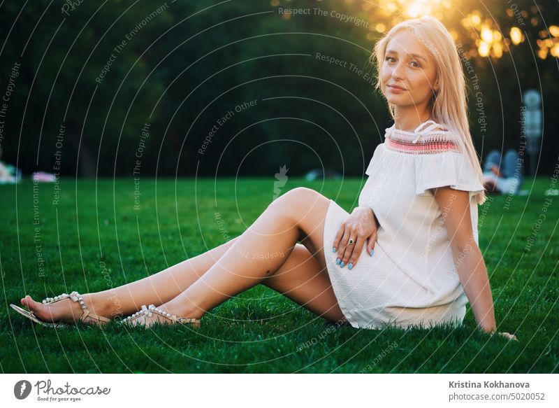 Beautiful blonde woman sitting on green grass in park at summer and looking at camera attractive beautiful beauty caucasian female girl happy lifestyle nature