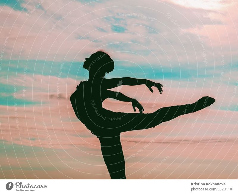 Silhouette of young woman ballerina or gymnast like a bird on dramatic sunset sky background. Ballerina practices in elegant moves. Concept of art, nature beauty