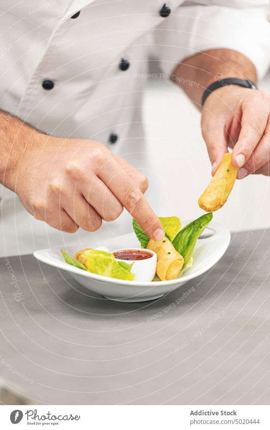 Professional chef serving spring rolls on plate professional dish herbs fancy sauce restaurant kitchen table man white chef jacket young adult food cuisine cook