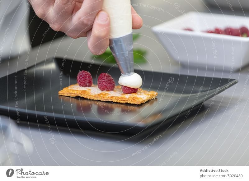 Professional chef making dessert with berries and frosting professional piping bag dish fancy plate raspberry table man white sweet chef jacket young adult food