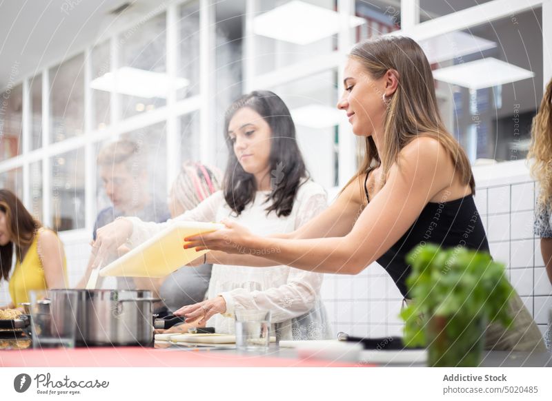 Positive women cooking in steaming pot at workshop adding ingredient positive diligent casual cutting board cookery stainless kitchen table professional