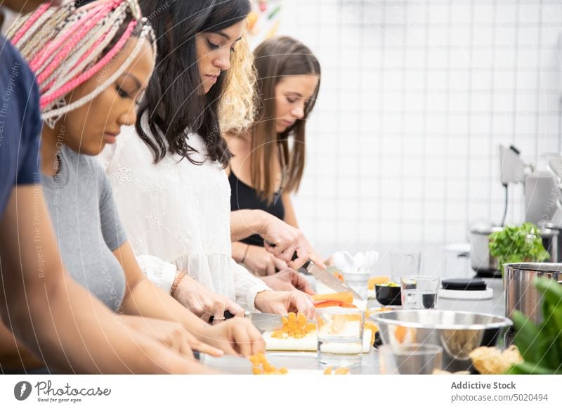 Multiracial people learning how to cut vegetables at cooking workshop attentive focused slicing knife cutting board together stand kitchen professional