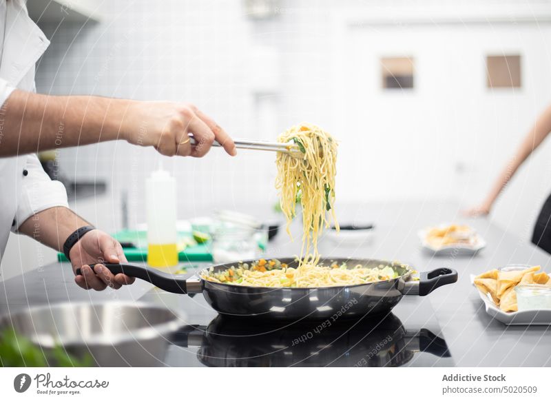 Crop man in white chef jacket catching spaghetti from the pan demonstrating dish serving cooking workshop professional restaurant kitchen showing young adult