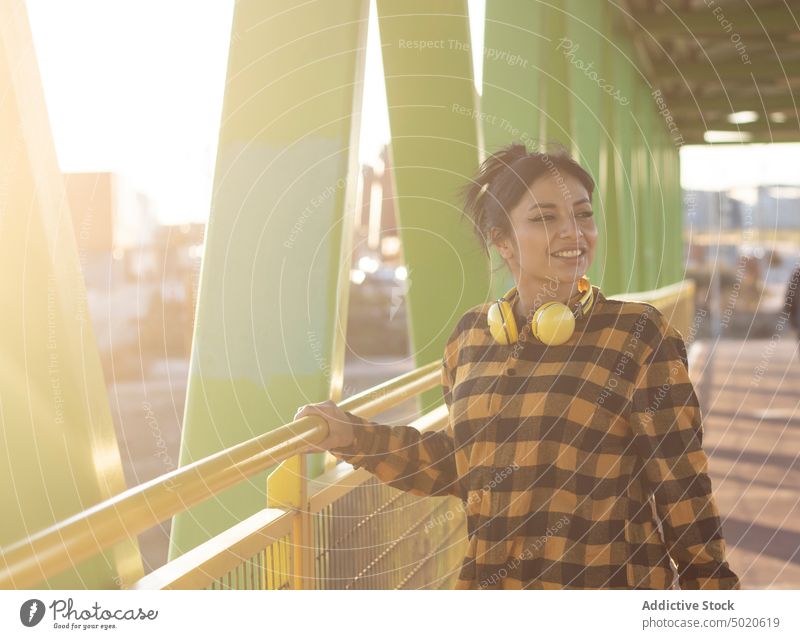 Happy young Latin American lady smiling while standing on bridge in town woman smile happy style promenade optimist positive sunlight enjoy glad delight female