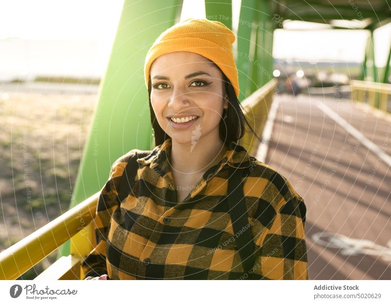 Happy young Latin American lady smiling while standing on bridge in town woman smile happy style promenade optimist positive sunlight enjoy glad delight female