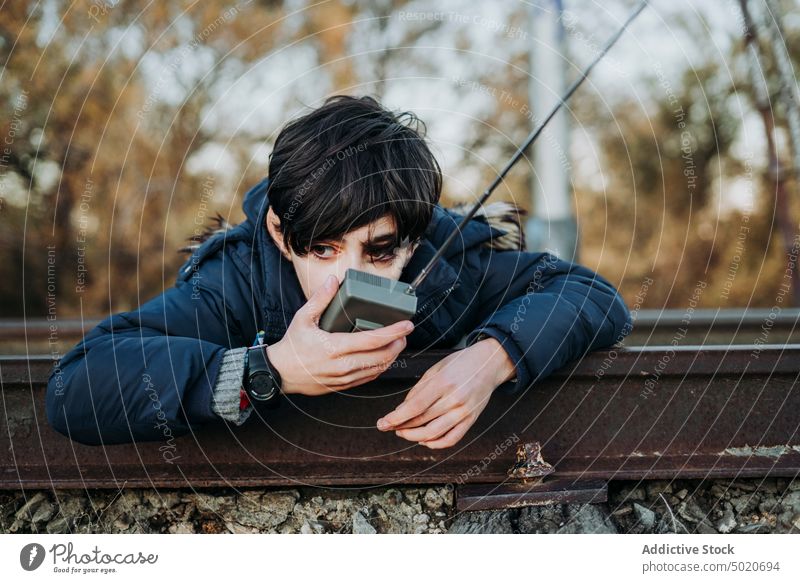 young child using a walkie-talkie lying on train tracks boy male communication playground playing green children portrait blue radio cute fun childhood outdoors
