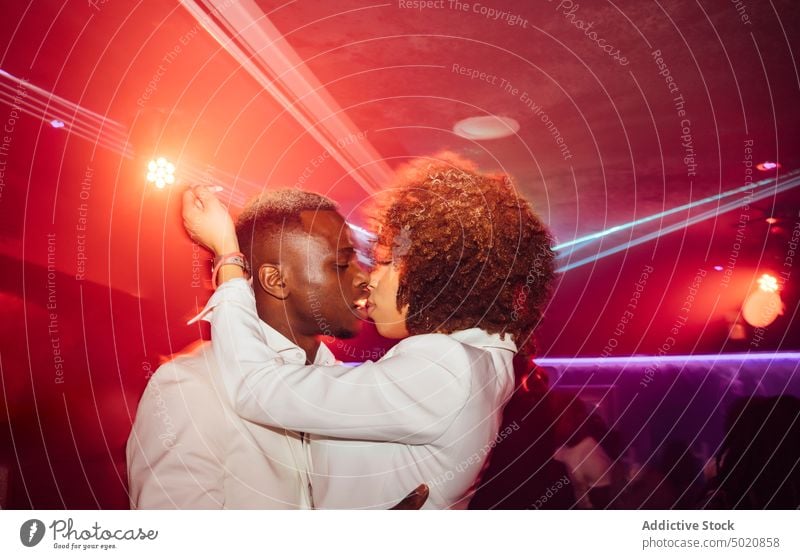 Black couple kissing during dance party nightlife hug ethnic neon illuminate entertain man woman lifestyle joy together celebrate event modern nightclub bright