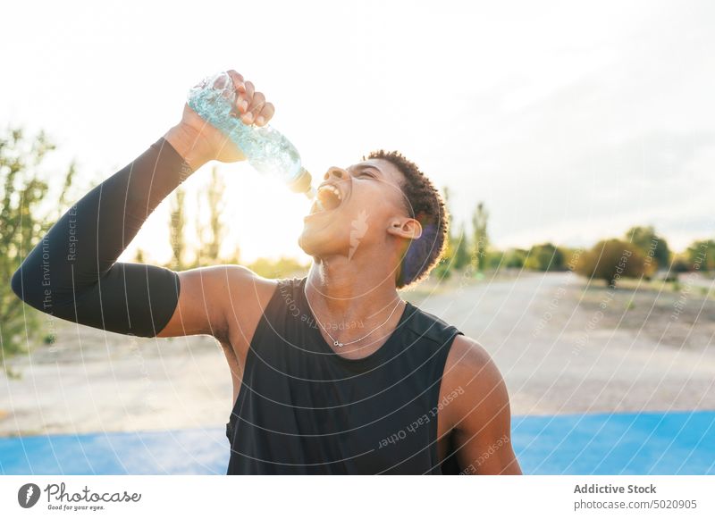 Black sportsman drinking water from bottle on playground thirsty healthy training young male athlete workout sportswear active sporty muscular black