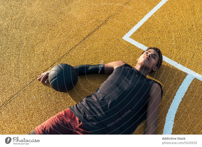 Calm black athlete lying down with ball on playground sportsman sitting player sportswear tired having rest field male powerful stadium professional young