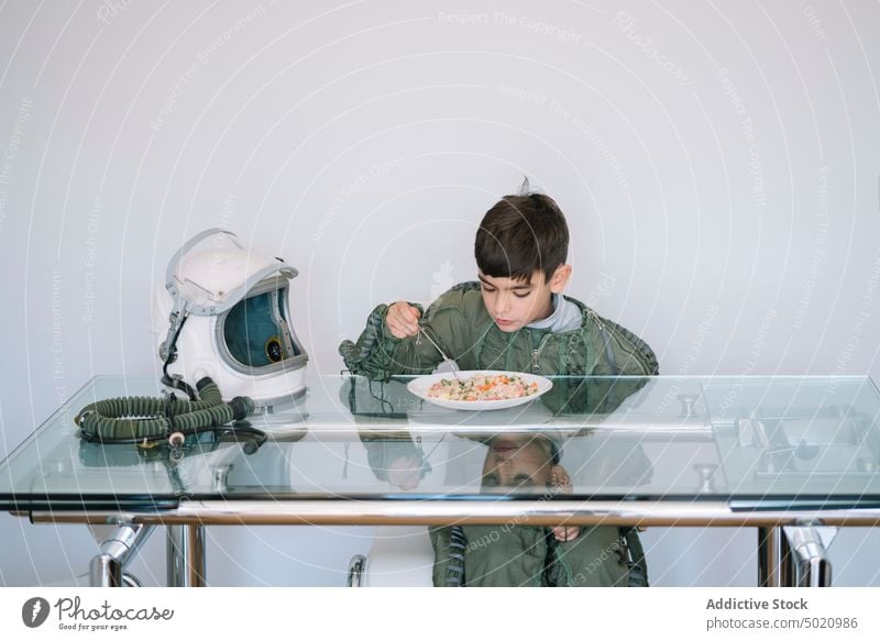 Boy dressed in an astronaut costume sitting at the table eating background boy child childhood concept creation handmade helmet imagination imaginative indoors