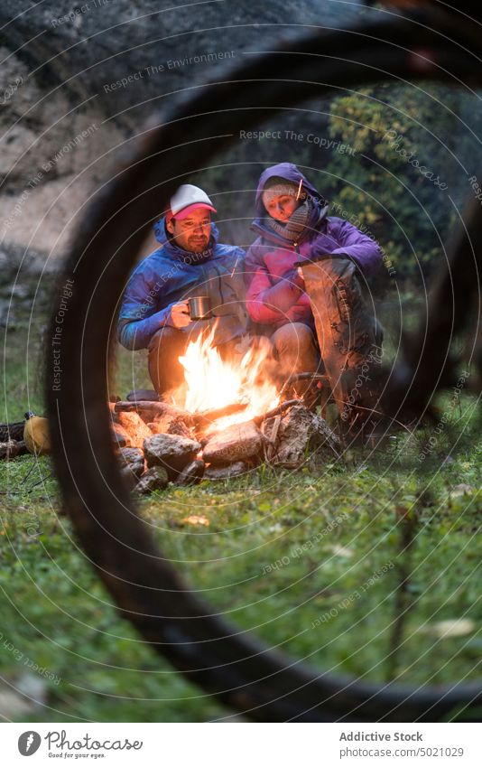 People in warm wear sitting by fire having warm beverage on a mug people bike flame adventure together bicycle heat friendship active fireplace nature hide