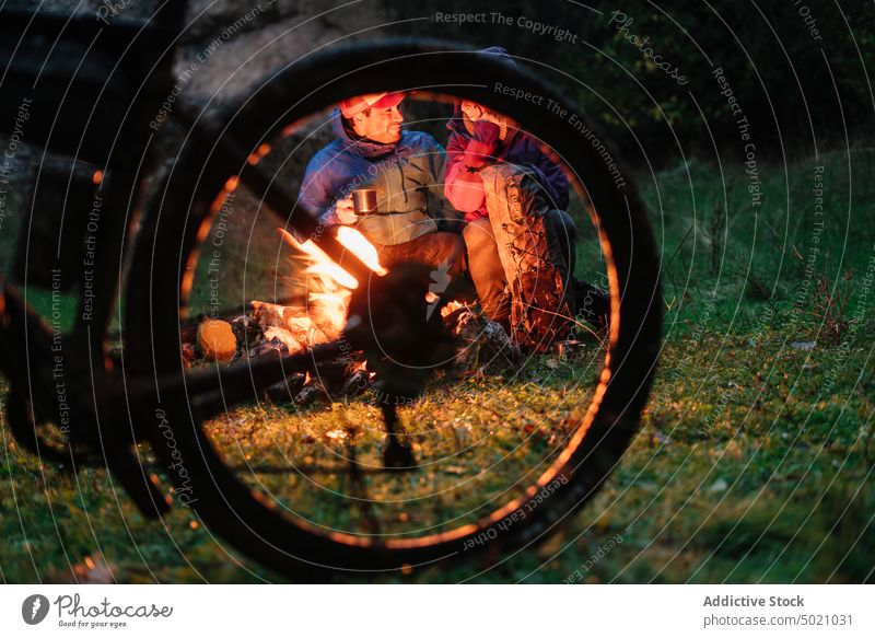 People in warm wear sitting by fire having warm beverage on a mug people bike flame adventure together bicycle heat friendship active fireplace nature hide