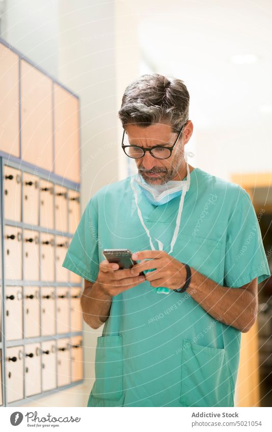 Serious surgeon using smartphone hospital serious corridor man adult doctor medicine healthcare break uniform technology device gadget browsing social media