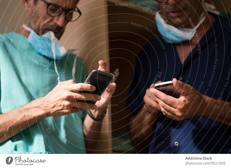 Surgeons using smartphones together surgeons hospital office doctors clinic healthcare men team uniform medicine technology device gadget browsing social media