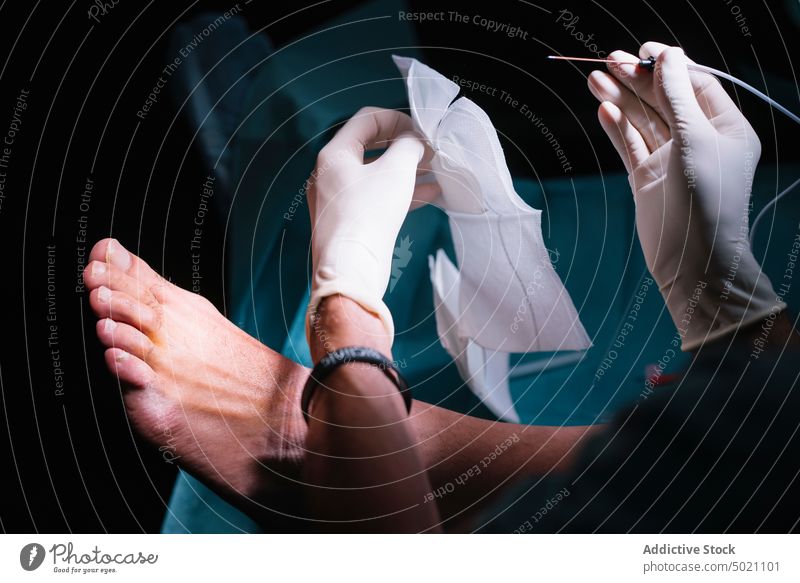 Crop hands inserting needle in patient feet surgeon gloves tool medicine hospital health treatment procedure equipment man professional emergency latex