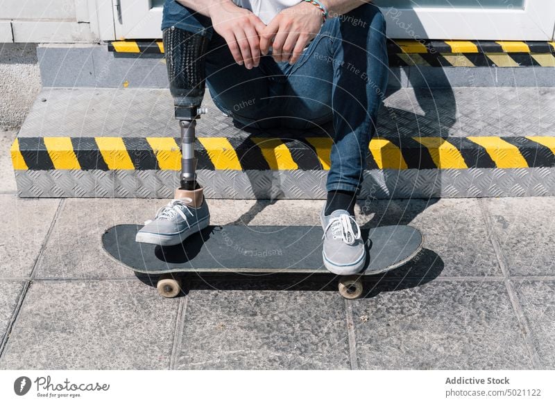 Crop skater with leg prosthesis sitting on stairs man skateboard artificial street city young urban male modern sunny daytime break hobby handicapped guy limb