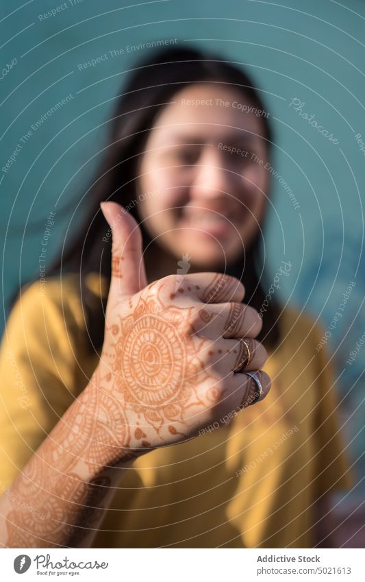 Content woman with mehndi hands showing thumb up gesture henna creative sign content female asian ethnic india art paint demonstrate street city inspiration