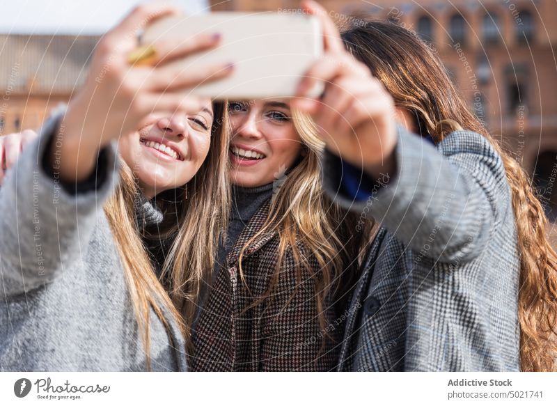 Company of women taking selfie along square in city smartphone together style friendship carefree using female mobile phone self portrait smile enjoy friendly