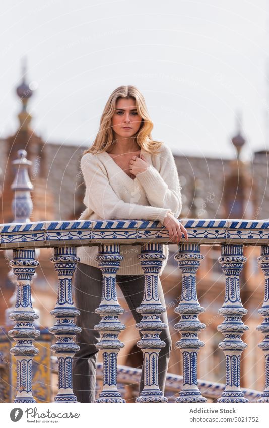 Stylish woman standing on footbridge in city style trendy unemotional seville plaza de espana spain female young enjoy urban emotionless positive blonde outfit